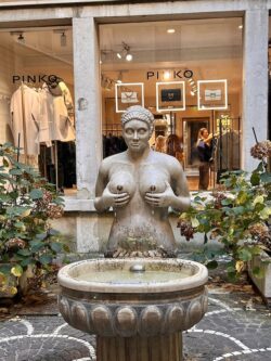 a stone fountain of a woman in Italy where the water and wine are spurted from her bosom