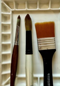 three paint brushes on a ceramic palette